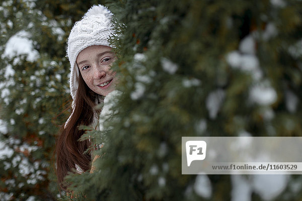 Portrait of Caucasian girl hiding behind tree in winter