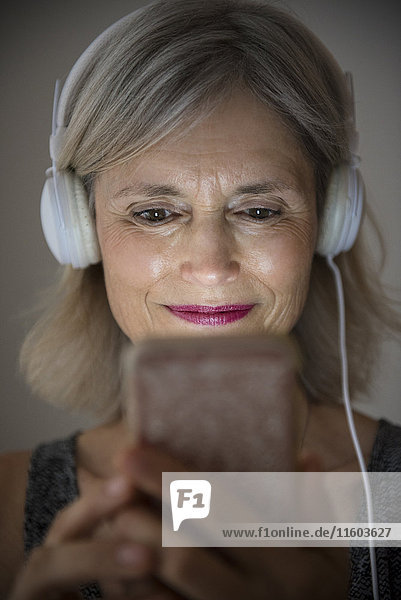 Lächelnde kaukasische Frau  die mit ihrem Mobiltelefon Musik hört