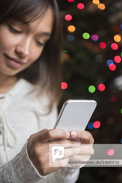 Mixed Race woman texting on cell phone near Christmas tree