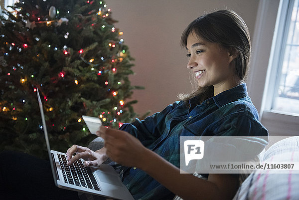 Mixed-Race-Frau beim Online-Shopping mit Laptop in der Nähe des Weihnachtsbaums