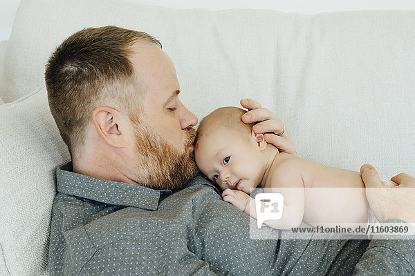 Father laying on sofa kissing baby daughter on head
