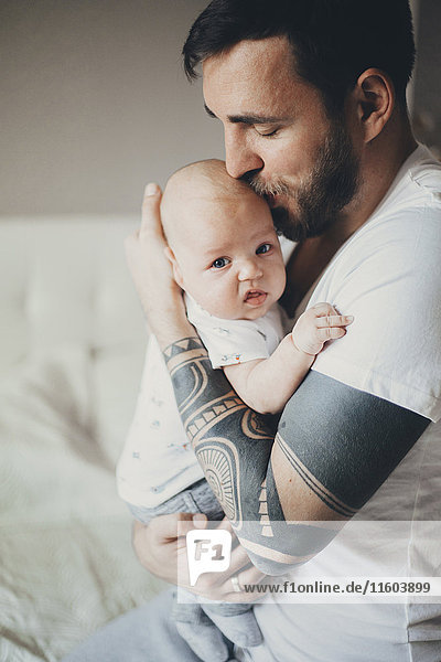 Caucasian father with tattoos on arms kissing baby son