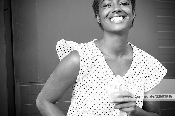 Lächelnde afroamerikanische Frau mit Mobiltelefon in der Hand