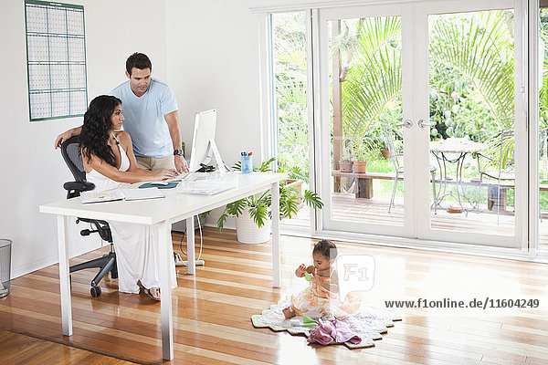 Mixed Race mother and father using computer and watching baby daughter