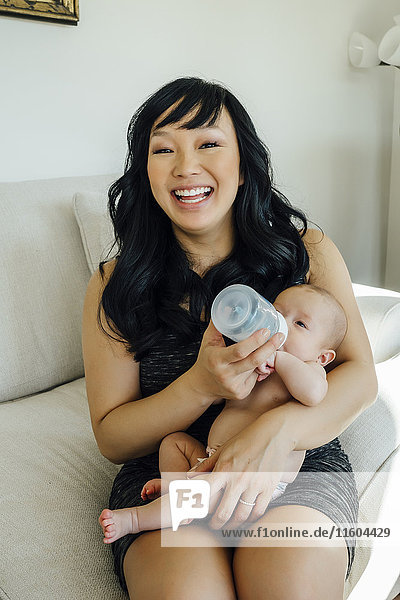 Porträt einer lächelnden Mutter  die ihre kleine Tochter mit der Flasche füttert