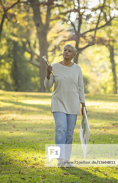 Nachdenkliche schwarze Frau mit Pinseln und Leinwand im Park
