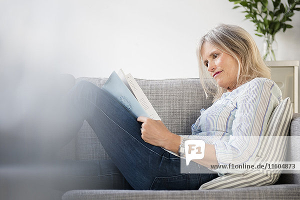 Ernste kaukasische Frau sitzt auf dem Sofa und liest Papierkram