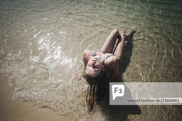 Kaukasische Frau im Bikini sitzt in den Wellen am Strand
