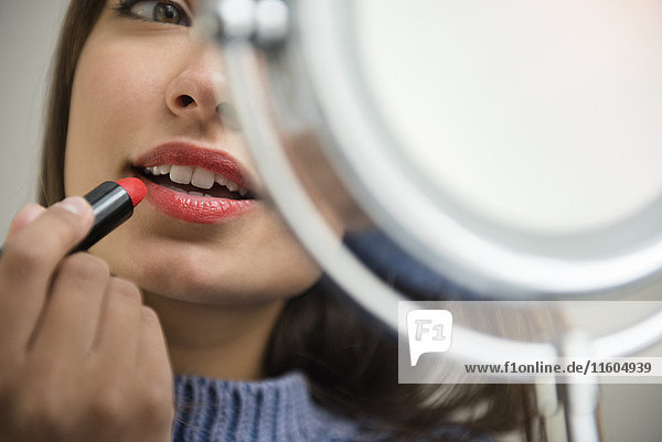 Gemischtrassige Frau trägt Lippenstift im Spiegel auf