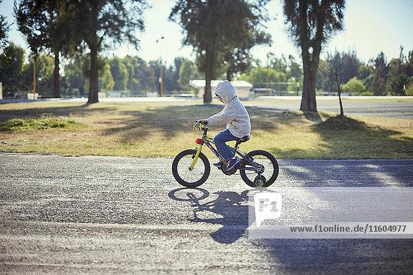 Hispanischer Junge fährt Fahrrad mit Stützrädern