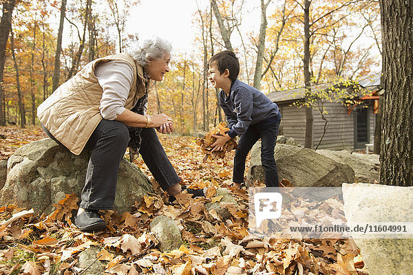Großmutter und Enkel spielen mit Herbstblättern