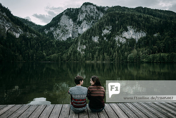 Kaukasisches Paar sitzt auf dem Steg in der Nähe der malerischen Aussicht auf einen Berg