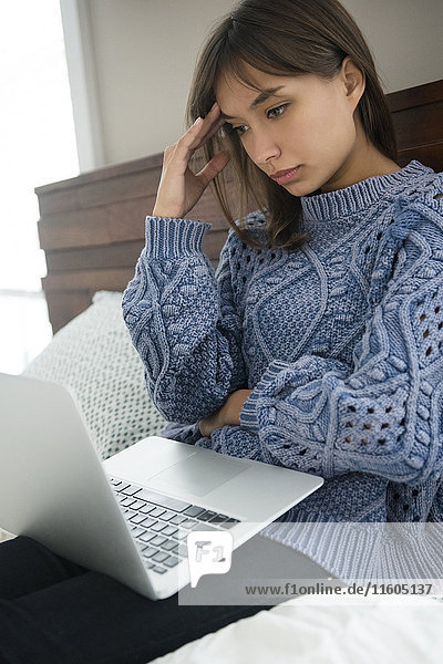 Frustrierte gemischtrassige Frau benutzt Laptop im Bett