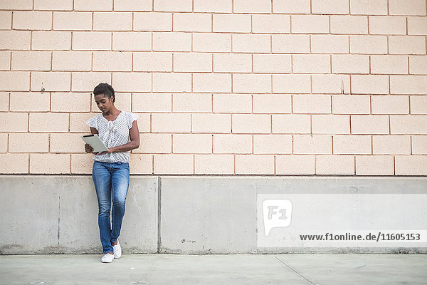 African American woman leaning on concrete wall using digital tablet