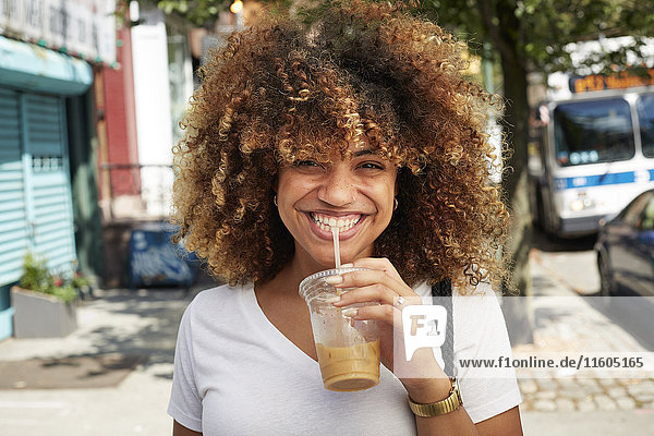 Black woman drinking with straw on city sidewalk