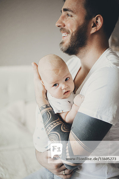 Caucasian father with tattoos on arms holding baby son