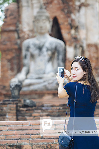 Asian woman photographing Buddha statue with cell phone