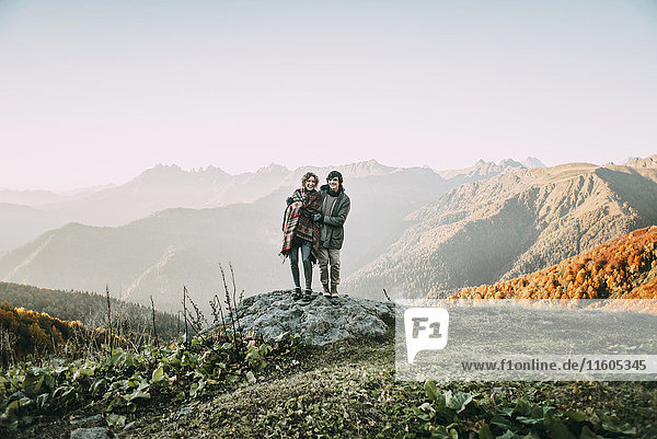 Kaukasisches Paar steht auf einem Bergfelsen mit Blick auf ein Tal