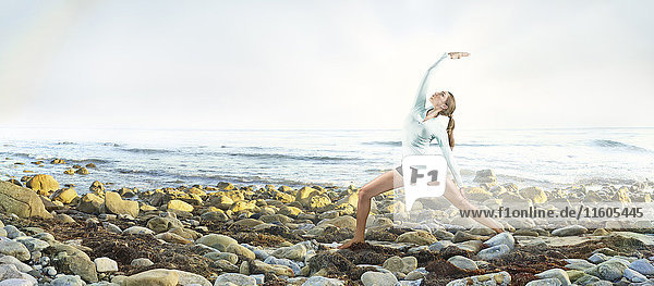 Gemischtrassige Frau übt Yoga am felsigen Strand