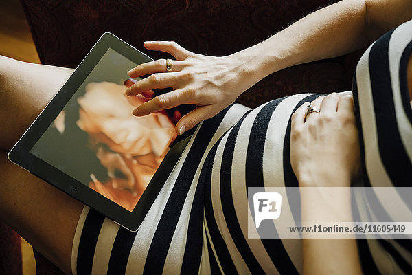 Mittelteil einer schwangeren kaukasischen Frau mit digitalem Tablet