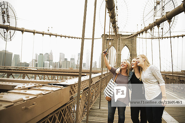 Lächelnde kaukasische Frauen posieren für ein Handy-Selfie auf einer Brücke