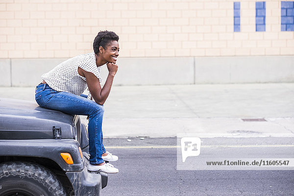 Lächelnde afroamerikanische Frau auf der Motorhaube eines Autos sitzend