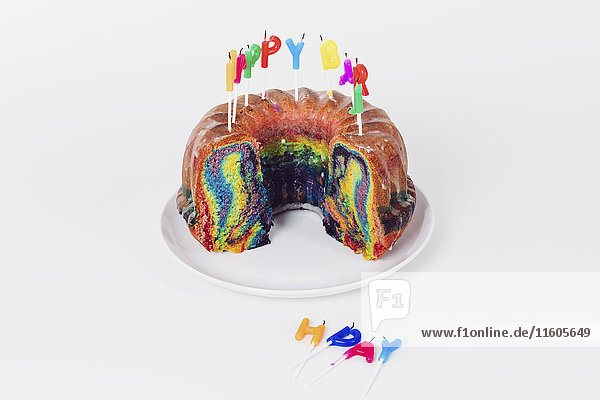 Geburtstagskerzen auf Regenbogenkuchen vor weißem Hintergrund