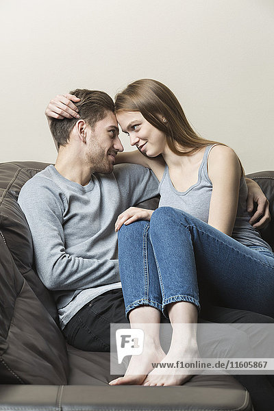 Liebenswertes junges Paar auf Sofa vor weißem Hintergrund