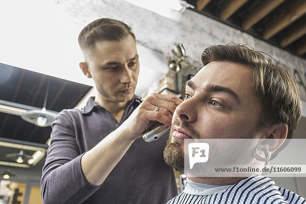 Low angle view of male hairdresser cutting young customer's hair at barber shop