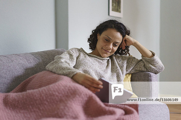 Smiling woman using digital tablet while relaxing on sofa at home