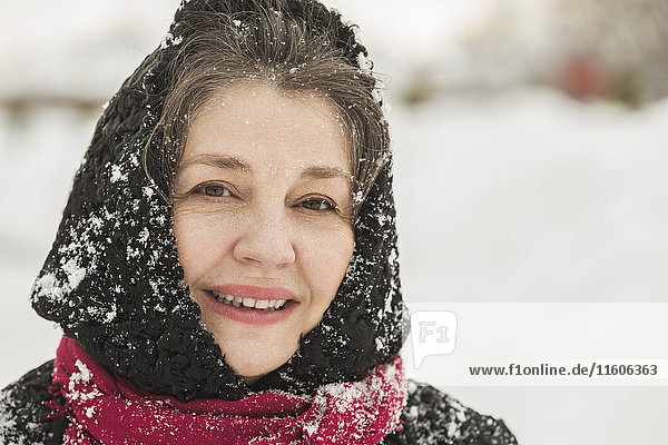 Porträt der lächelnden Seniorin im Winterkleid mit Schnee bedeckt