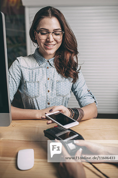 Happy young woman using smart phone to pay at counter