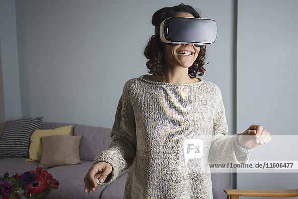 Glückliche Frau  die im Wohnzimmer steht und ein Virtual-Reality-Headset benutzt.
