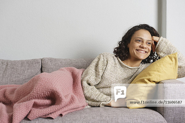 Nachdenkliche Frau lächelt und entspannt auf dem Sofa zu Hause