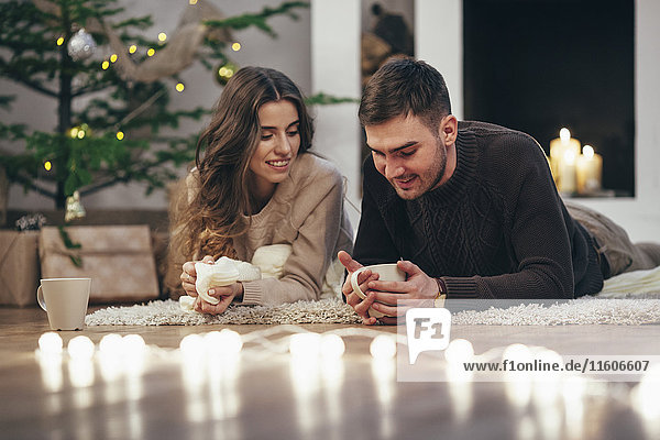 Lächelndes Paar beim Kaffeetrinken auf dem Teppich zu Hause zu Weihnachten