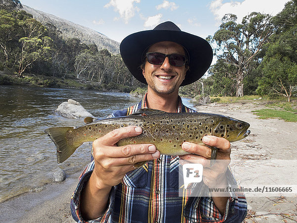 Porträt eines glücklichen reifen Mannes mit Fisch am Fluss  Jindabyne  New South Wales  Australien