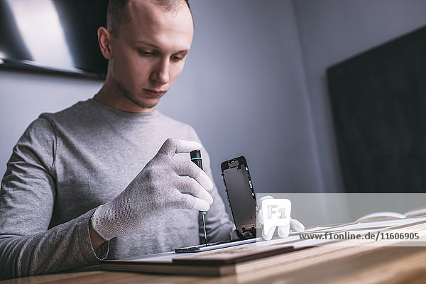 Young male technician repairing smart phone at electronics store