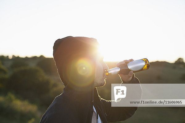 Seitenansicht des Mannes mit Biertrinken auf dem Feld bei Sonnenschein