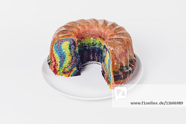 Hochwinkelansicht des Regenbogenkuchens im Teller auf weißem Hintergrund