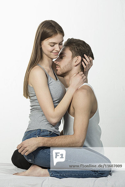 Romantic couple embracing while sitting on bed against white background