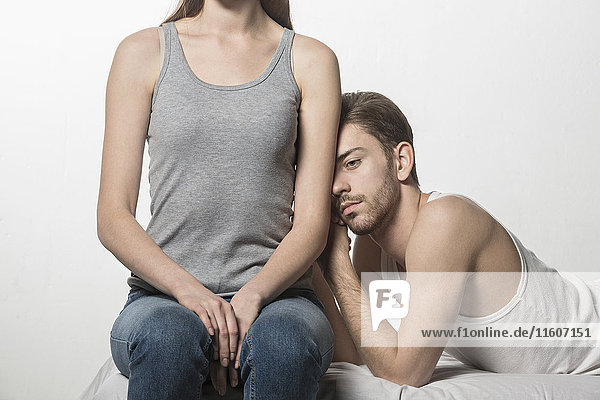 Thoughtful man leaning on girlfriend sitting at bed against white background