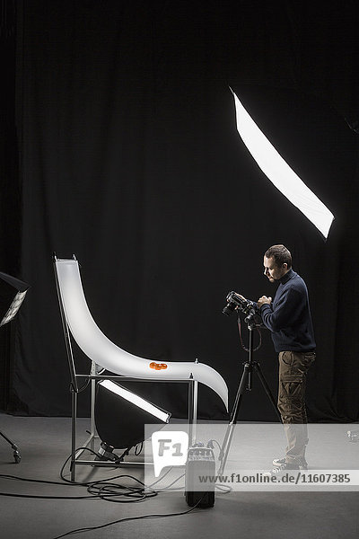 Volle Länge des Fotografen  der Essen im Studio vor schwarzem Hintergrund fotografiert.
