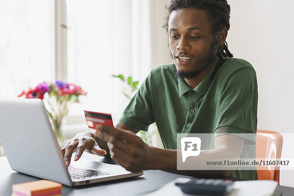 Young man shopping online through laptop and credit card at home