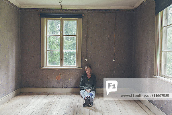Porträt einer selbstbewussten Frau  die zu Hause auf dem Parkettboden sitzt.