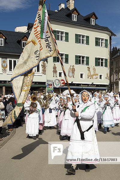 Aussee Karneval  Mann mit Maske schwingende Fahne  hinten Männer mit Masken und Instrumenten  weiße Gewänder  Trommelweiber  Bad Aussee  Steiermark  Österreich  Europa