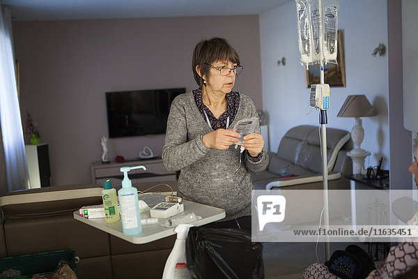 Reportage über einen häuslichen Pflegedienst in Savoie  Frankreich. Eine Krankenschwester wechselt bei einem Krebspatienten den Beutel für parenterale Ernährung.
