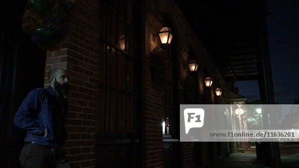 Mann lehnt sich gegen ein Backsteingebäude mit flackernden Lichtern bei Nacht