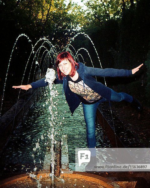 Frau balanciert auf einem Bein am Wasserbrunnen