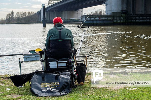 Rotterdam  Netherlands. Senior adult and retired male fishing for relaxation at the banks of Nieuwe Maas River  just under Van Brienenoordbrug at highway A16.