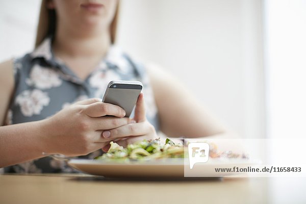 Woman using smartphone with plate of food in foreground.